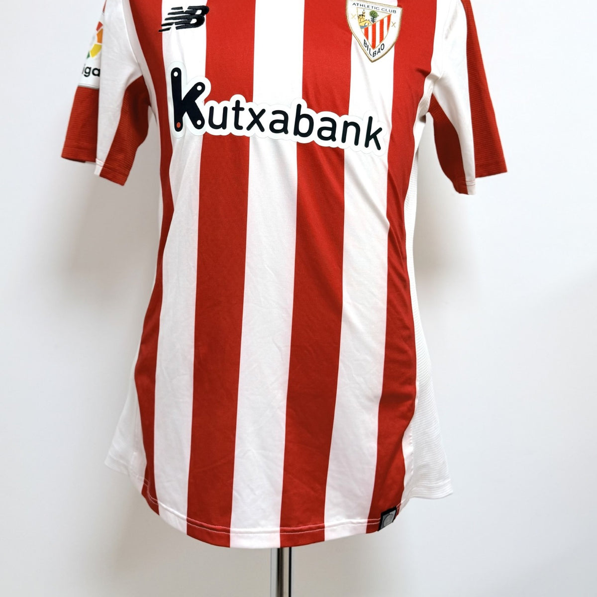 Vista anterior completa, se aprecia el tipo de cuello, escudo, logo marca NB y sponsor Kutxabank