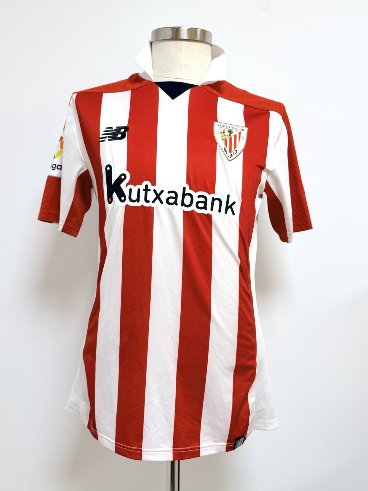 Vista anterior completa, se aprecia el tipo de cuello, escudo, logo marca NB y sponsor Kutxabank
