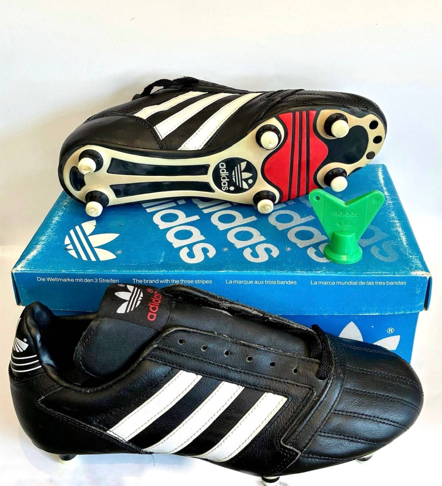 Vista de las botas adidas Milano Super de 1987. La bota izquierda se muestra sobre la caja original.